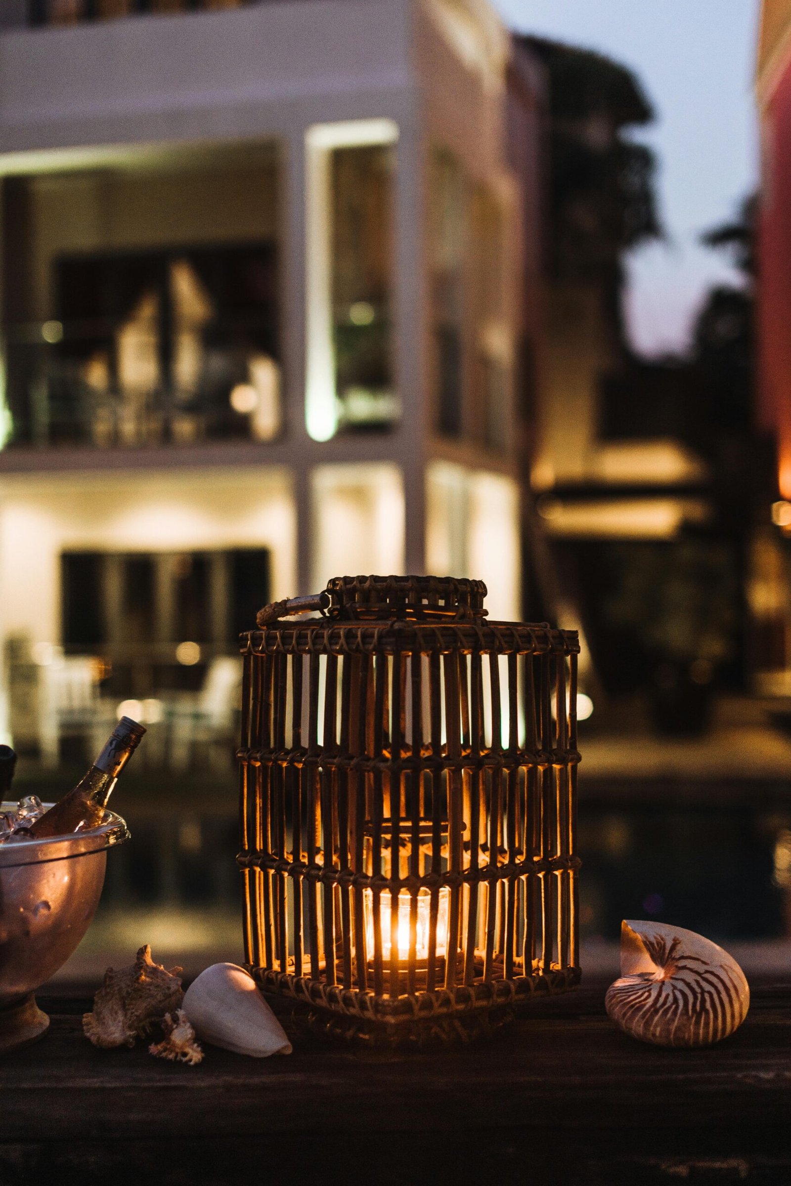 A warm lantern and seashells create an inviting ambiance at a stylish poolside setup during twilight.